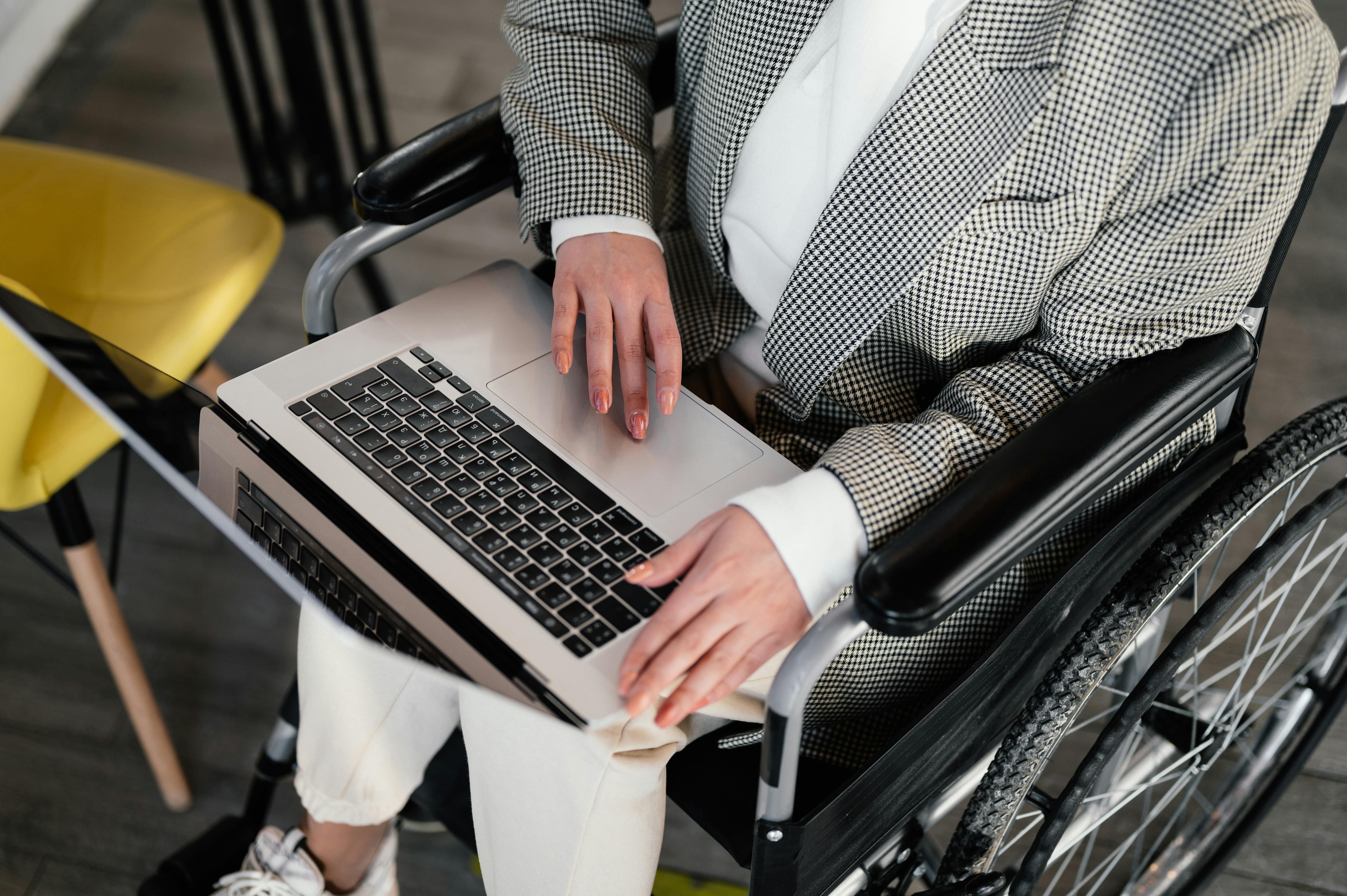 personne non identifiée positionnée dans un fauteuil roulant qui regarde un ordinateur portable