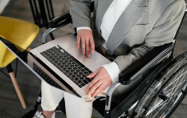 personne non identifiée positionnée dans un fauteuil roulant qui regarde un ordinateur portable
